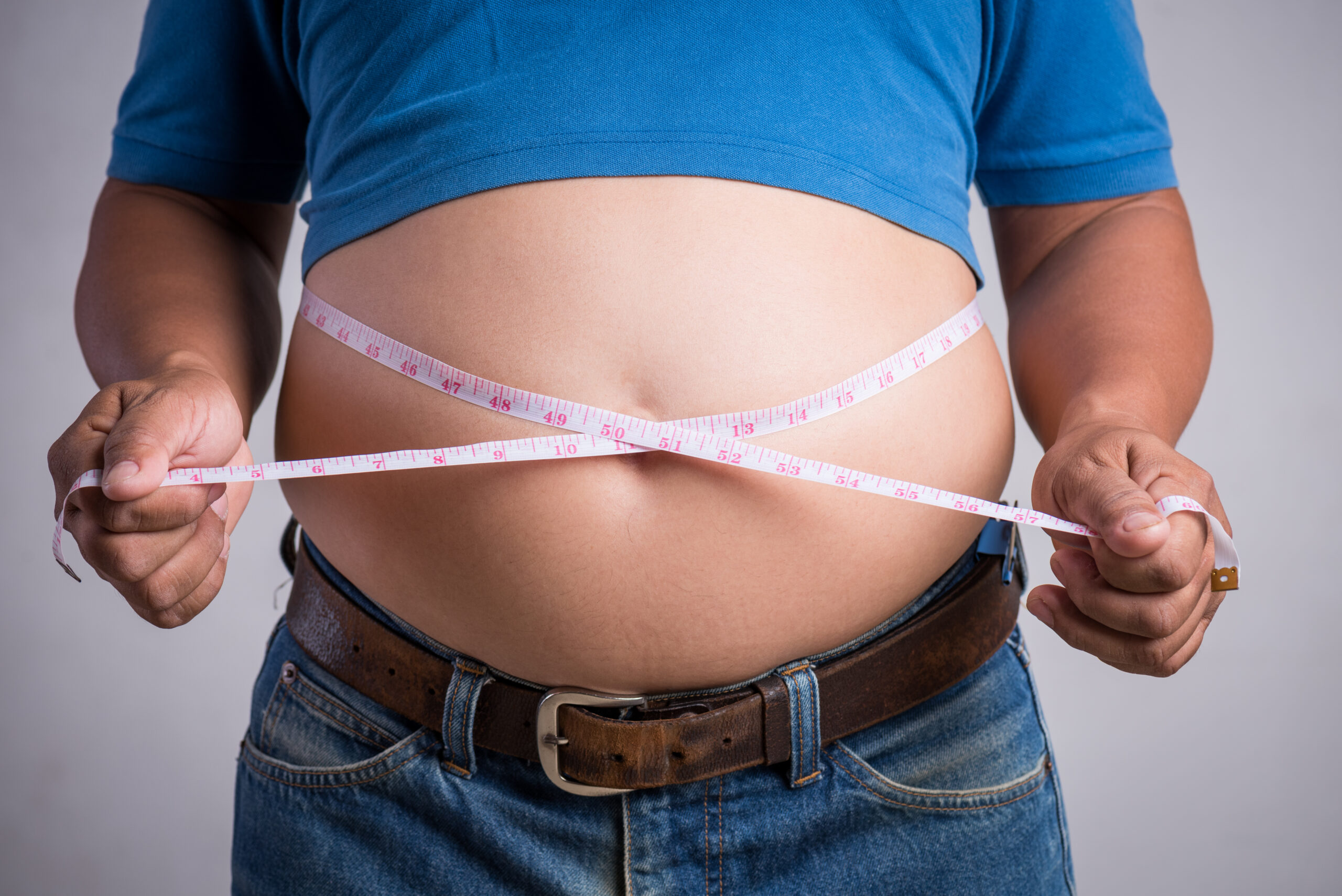 Overweight or fat adult man in very tight jeans with measuring t